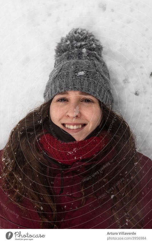 Porträt junge Frau im Schnee, trägt eine graue Mütze und einen roten Mantel. Er lächelt und schaut in den Himmel hübsch Nahaufnahme Markt Kapuze Mode Glück