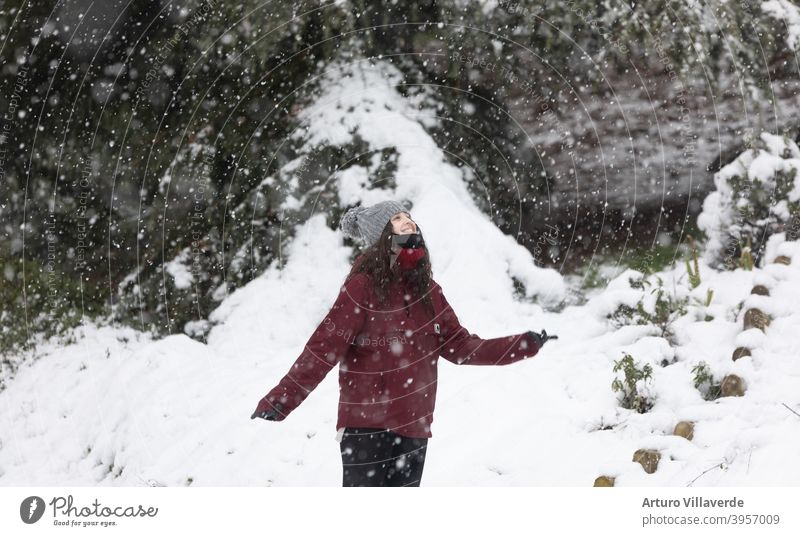 junge Frau im Schnee, trägt eine graue Mütze und einen roten Mantel. Er lächelt und blickt in den Himmel hübsch Nahaufnahme Markt Kapuze Mode Glück Schlag