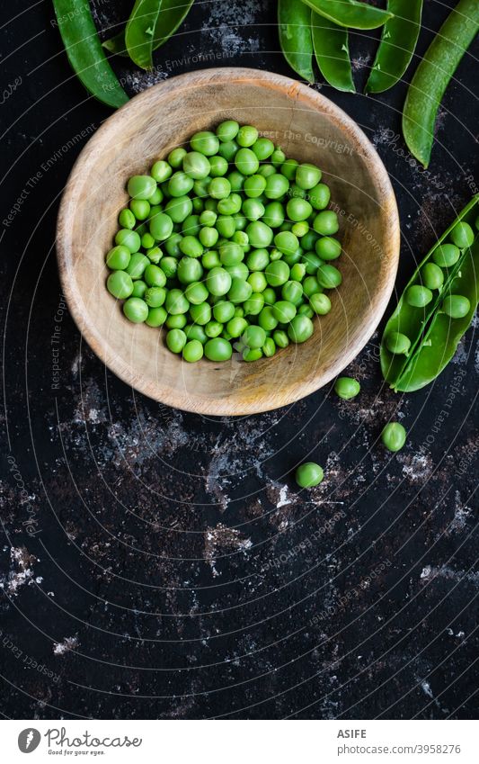 Grüne Erbsen in einer Schüssel und Schoten auf einem rauen dunklen Hintergrund grüne Erbsen roh frisch Hülse Gemüse Gesundheit Lebensmittel angeblättert