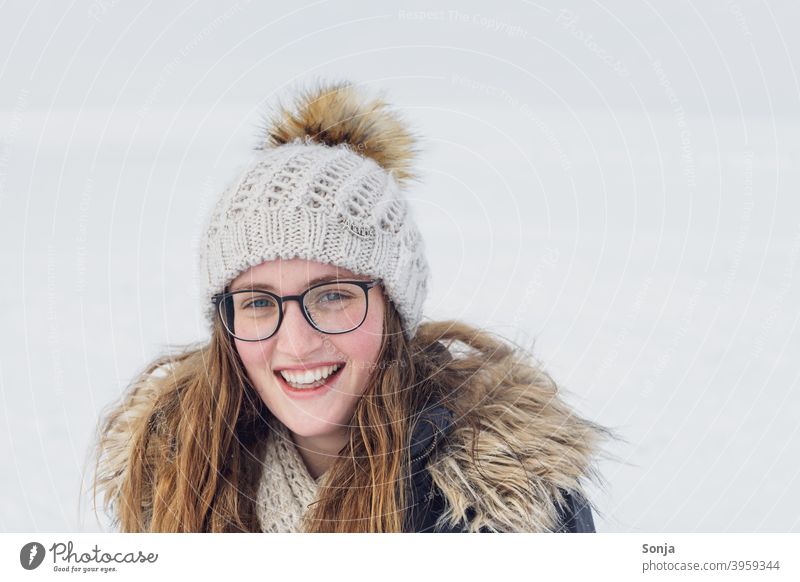 Junge lächelnde Frau mit Brille und Wollmütze jung Lächeln Winter Schnee lange Haare lockig brünett Porträt sehen Freude hübsch schön natürlich Gesicht