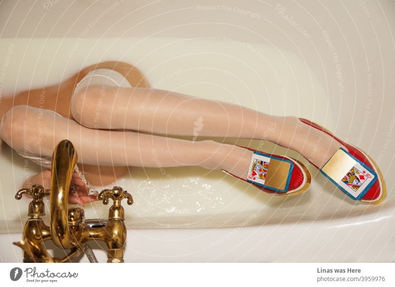 Lange Beine einer Frau sind das Hauptmotiv dieses Bildes. Sie entspannt sich in einem Milchbad mit ihren roten Avantgarde-Schuhe an. Goldene Karten und goldenen Kran begleiten sie mit diesen High-Fashion-Schuhe.