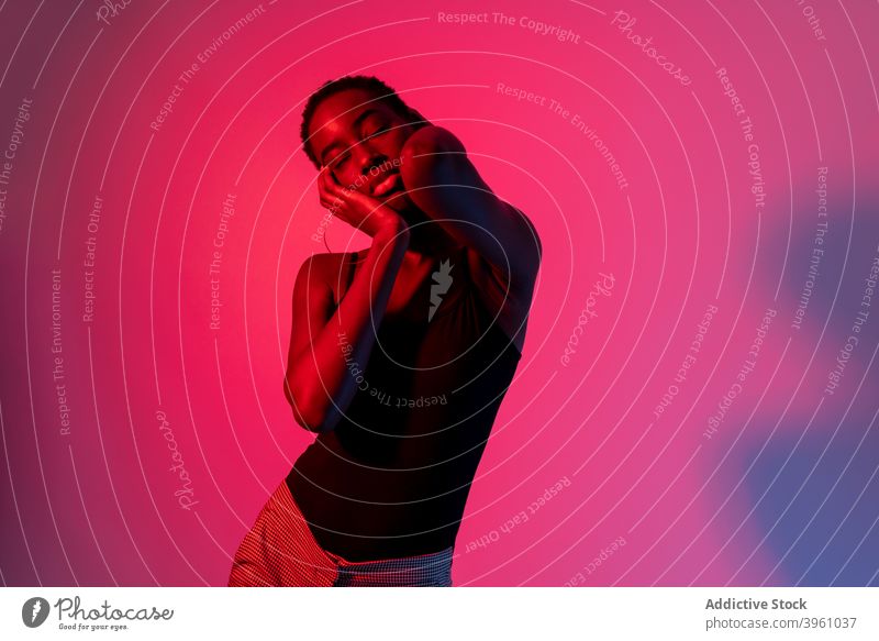 Verführerische junge schwarze Dame berühren Gesicht mit geschlossenen Augen in neon rosa Studio Frau Gesicht berühren Augen geschlossen selbstsicher Verlockung