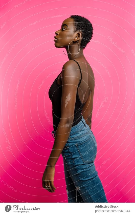 Junge schwarze Frau steht in rosa Studio selbstbewusst Model Porträt positiv selbstsicher Stil jung Afroamerikaner ethnisch passen Top Jeanshose trendy Freude