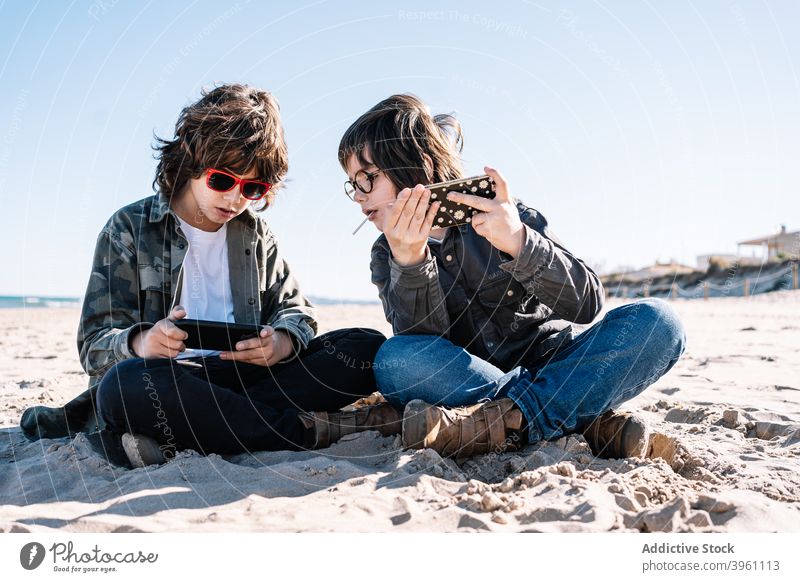 Zwei Kinder spielen mit ihrem Handy am Strand Junge Smartphone authentisch aktiv Pause Küste Konzept Spaß Feiertag Lifestyle Natur im Freien außerhalb Menschen