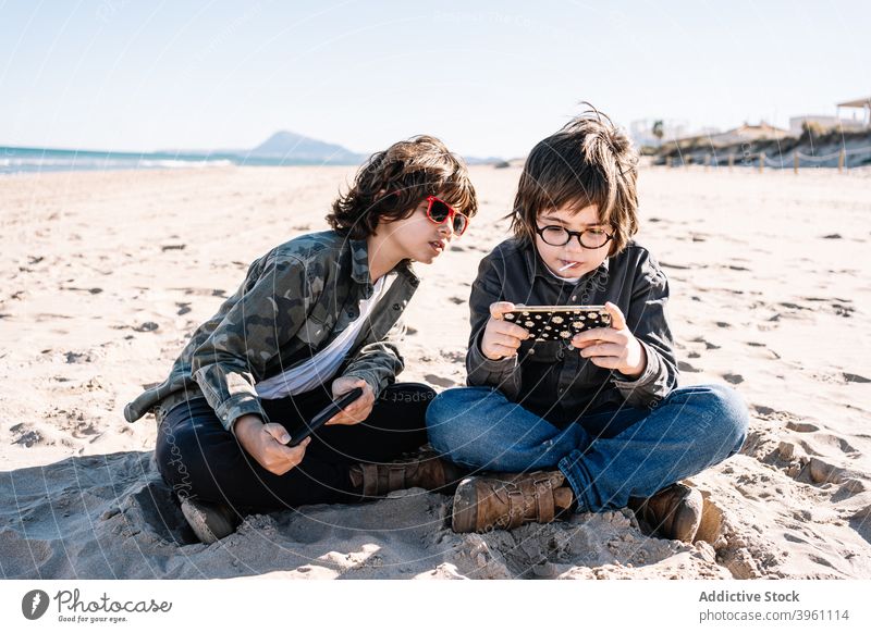 Zwei Kinder spielen mit ihrem Handy am Strand Junge Smartphone authentisch aktiv Pause Küste Konzept Spaß Feiertag Lifestyle Natur im Freien außerhalb Menschen