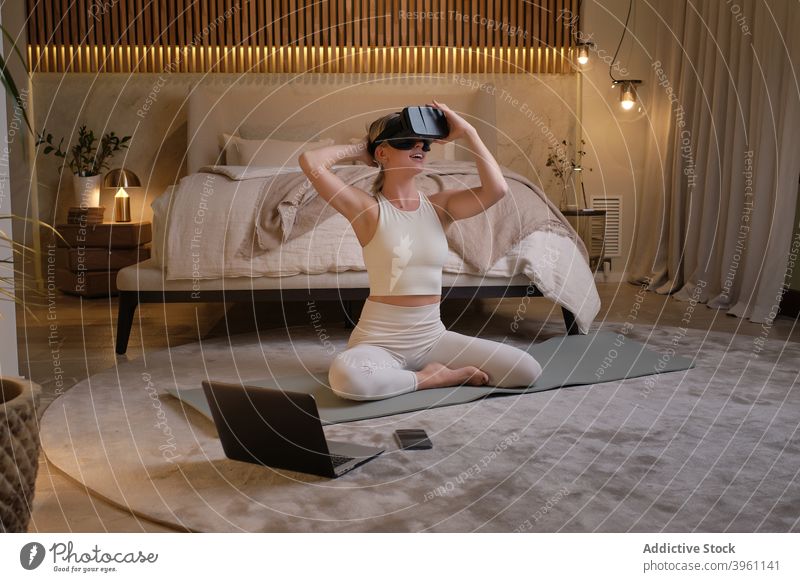 Frau mit VR-Brille macht Yogaiat zu Hause Virtuelle Realität online Tutorial Laptop üben Asana Lächeln Inhalt Pose heimwärts Achtsamkeit Unterlage Apparatur