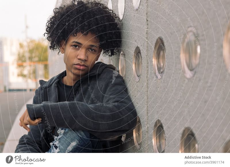 Teen ethnischen Mann mit lockigem Haar sitzen auf der Straße Hipster Teenager krause Haare urban ernst jung Afro-Look modern männlich Afroamerikaner schwarz