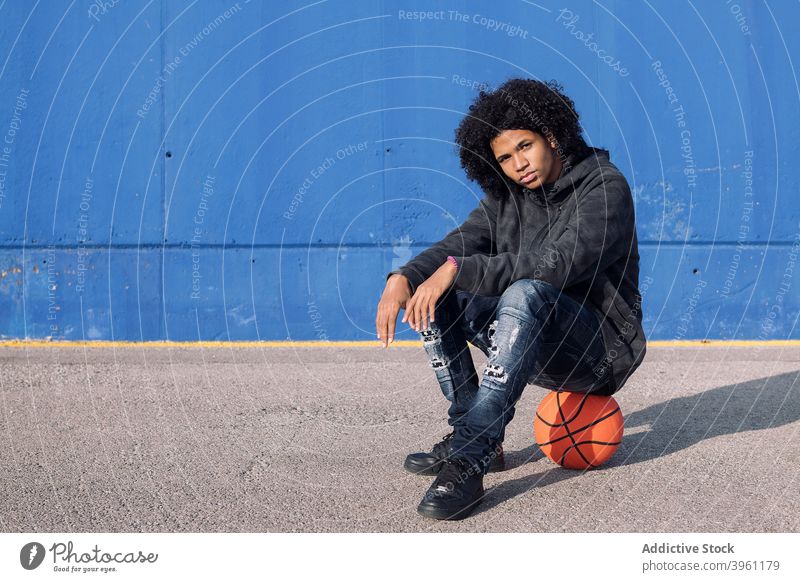 Hipster schwarzer Jugendlicher sitzt auf Basketball Mann Ball Teenager ernst Streetball jung selbstbewusst Stil männlich informell Afroamerikaner ethnisch
