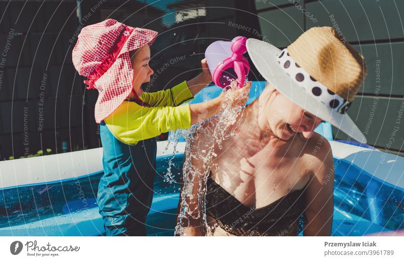 Baby gießt Wasser auf Mutter im Babyschwimmbad. Pool Sommer Kind Mädchen Spaß aufblasbar offen Lifestyle authentisch Sonne Schutz Hut Gießen Familie