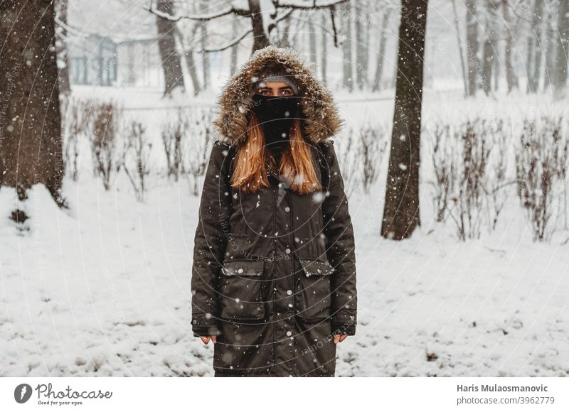Frau mit Gesichtsmaske steht im Freien im Schnee Erwachsener allein attraktiv schön schwarz brünett kalt selbstbewusst Coronavirus covid-19 niedlich Mode Wald