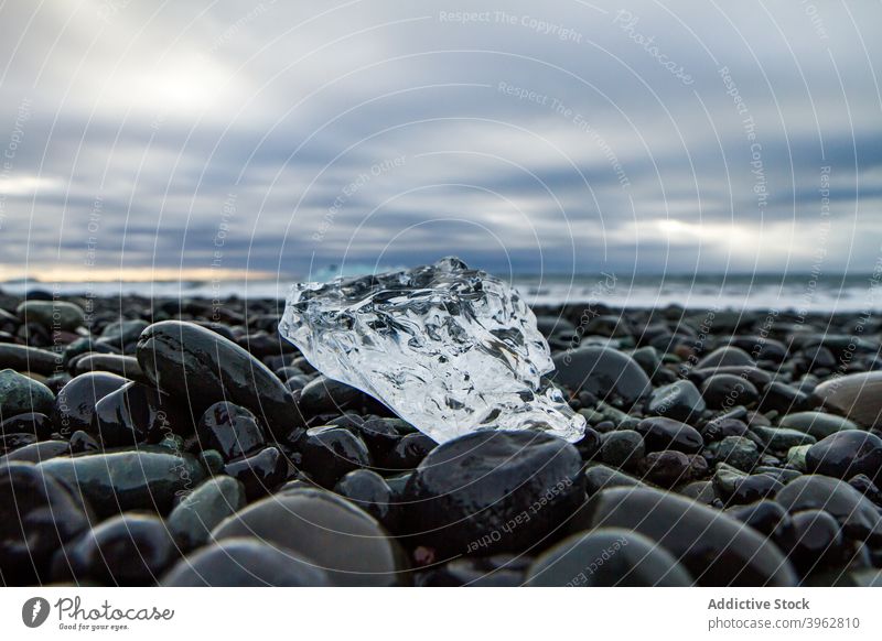 Eisstück auf steinigem Strand im Winter Spielfigur Chunk Meeresufer Seeküste gefroren frieren durchsichtig Island Kristalle wolkig Himmel arktische kalt Natur
