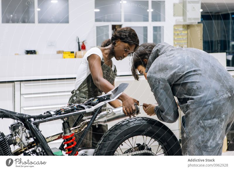 Mechaniker befestigen Auspuffanlage eines Motorrads zusammen fixieren Zusammensein Werkstatt System Schalldämpfer Reparatur multiethnisch rassenübergreifend