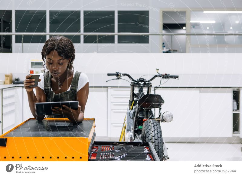 Schwarzer Mechaniker, der in einer Motorradwerkstatt auf einem Tablet surft Frau Werkstatt Browsen Tablette Arbeit Techniker trinken Kaffee ethnisch schwarz