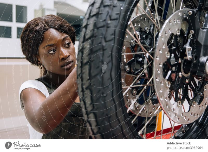 Professioneller weiblicher Meister, der das Rad eines Motorrads repariert Frau Mechaniker fixieren benutzerdefiniert Werkstatt professionell Arbeit Reifen