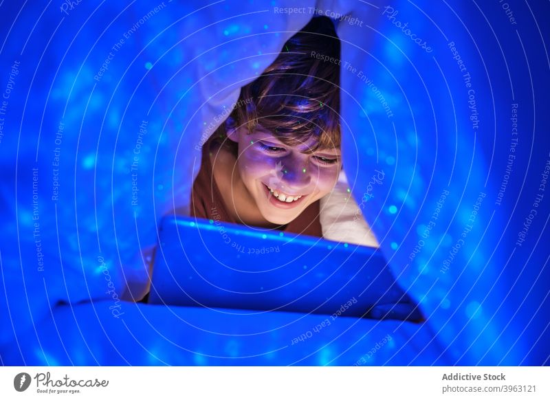 Inhalt Junge mit Tablet in dunklem Raum Tablette Browsen Kind heiter Bett Schlafzimmer Decke Tierhaut dunkel spielerisch Lächeln Internet Glück Gerät online