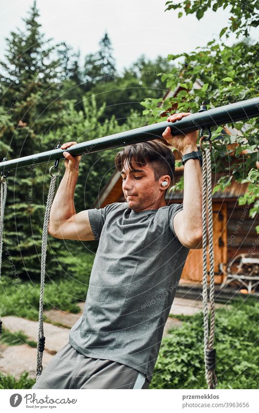 Junger Mann macht Klimmzüge an der horizontalen Klimmzugstange während seines Calisthenics-Trainings auf einem Campingplatz während seines Sommerurlaubs aktiv