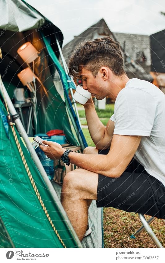 Junger Mann trinkt einen Kaffee sitzend vor dem Zelt am Morgen Abenteuer Getränk Pause Frühstück Lager Camping Nahaufnahme Tasse trinken Erkundung Freiheit
