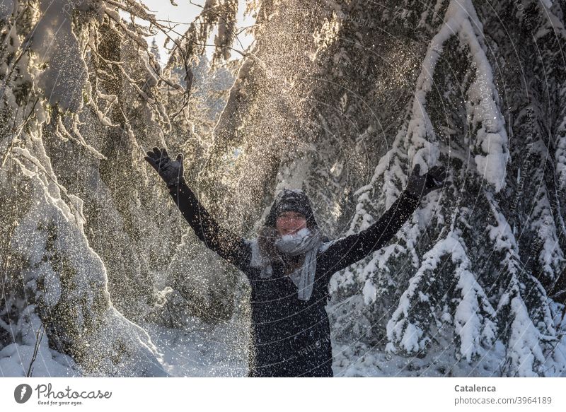 Die junge Frau freut sich über den Schneestaubschauer  der von den Tannen fällt und hebt die Arme Nadelholz Wald Wetter Witterung Winter Kälte Tag Tageslicht