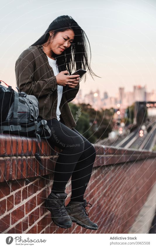 Ethnisch reisende Frau mit Smartphone in der Stadt Reisender Browsen Backpacker Großstadt Straße Lächeln Nachricht asiatisch ethnisch Australien Baustein Zaun