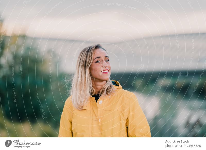 Fröhliche Frau im Park stehend gelb Regenmantel Lächeln Wochenende genießen Großstadt Oberbekleidung Outfit heiter Freude sorgenfrei Natur charmant Saison