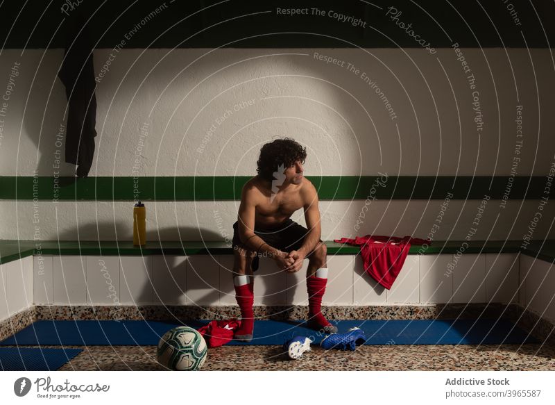 Ein Fußballspieler in der Umkleidekabine mit Sportuniform Mann Spieler sittimg Volk Ankleidezimmer Innenbereich Uniform Turnschuh Bank Sportbekleidung sportlich