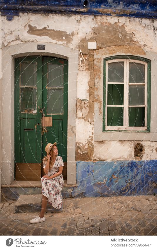 Weiblicher Reisender sitzt auf der Straße in der Nähe von alten Gebäude in Algarve Frau Haus sitzen Türschwelle Glück Sightseeing Sommer Feiertag heiter jung