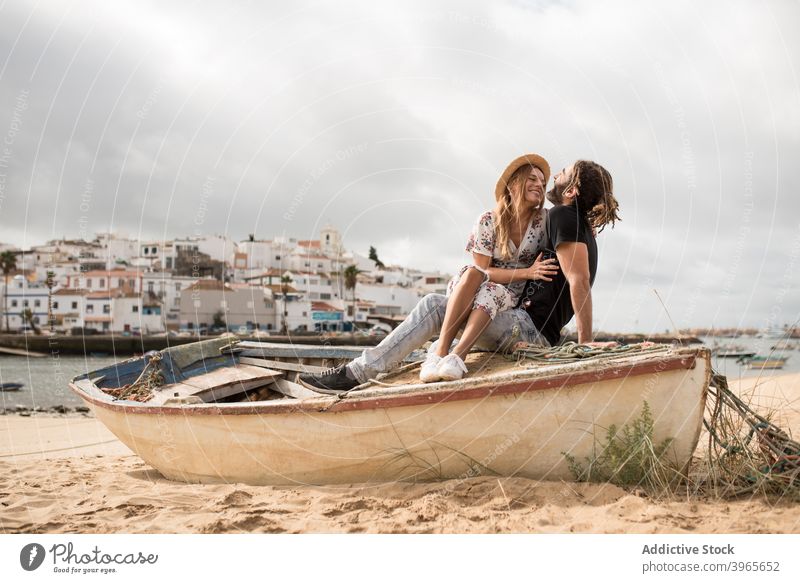 Glückliches reisendes Paar umarmt auf Holzboot auf sandigen Küste gegen bewölkten Himmel kuscheln Boot Strand Zusammensein romantisch Liebe Lächeln Feiertag