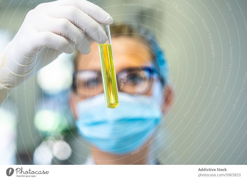 Wissenschaftlerin mit Reagenzglas im Labor Frau Flasche Chemikalie liquide Glas Probe Mundschutz Latex ernst Experiment farbenfroh verschiedenfarbig Arbeit