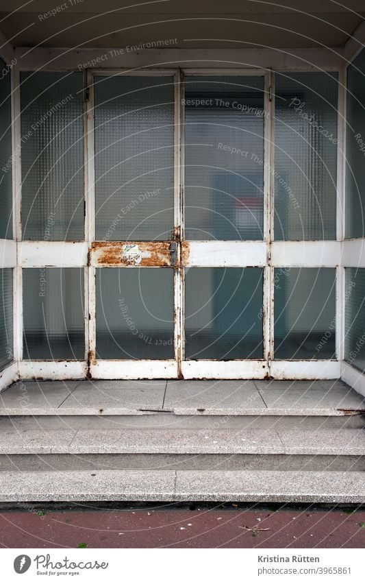 angerostete eingangstür glastür zugang türklinke rostig alt treppe stufen schule behörde amt gebäude architektur verwittert patina