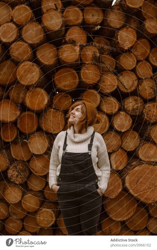 Frau steht in der Nähe von Stapel von Holzstämmen Totholz Haufen Kofferraum besinnlich nachdenklich hölzern warme Kleidung Lächeln jung Landschaft Lifestyle