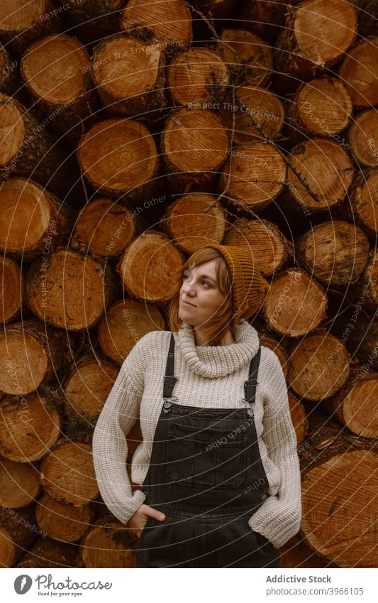 Frau steht in der Nähe von Stapel von Holzstämmen Totholz Haufen Kofferraum besinnlich nachdenklich hölzern warme Kleidung Lächeln jung Landschaft Lifestyle