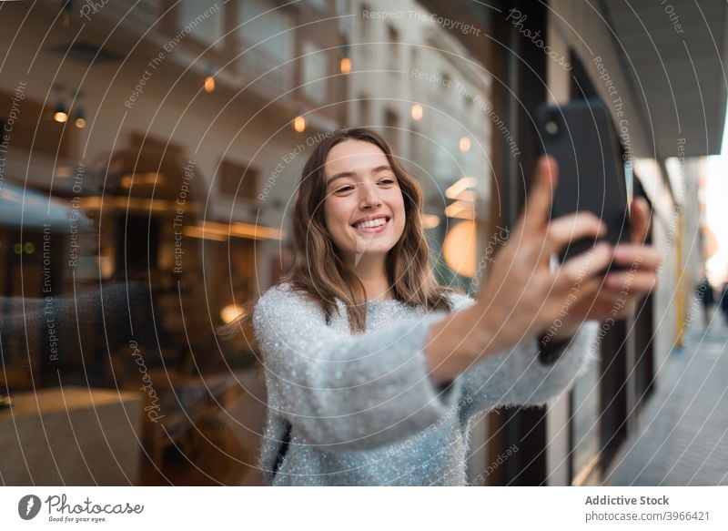 Fröhliche Frau nimmt Selfie auf Smartphone in der Stadt heiter Großstadt Wochenende Selbstportrait charmant Lächeln fotografieren Café Fenster Mobile Glück froh