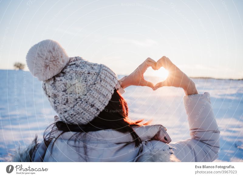glückliche junge Frau Wandern in verschneiten Berg bei Sonnenuntergang tun eine Herzform mit den Händen. Wintersaison. Natur und Liebe Schnee Rückansicht