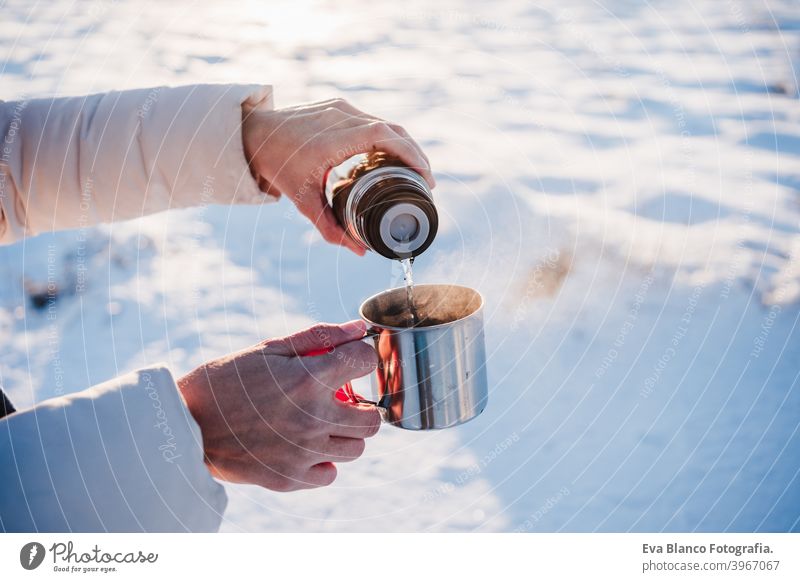 unerkennbar schöne junge Frau bei Sonnenuntergang in verschneiten Berg gießen heißen Tee aus Thermoskanne zu metallischen Tasse. Reisen und Natur Konzept. Wintersaison