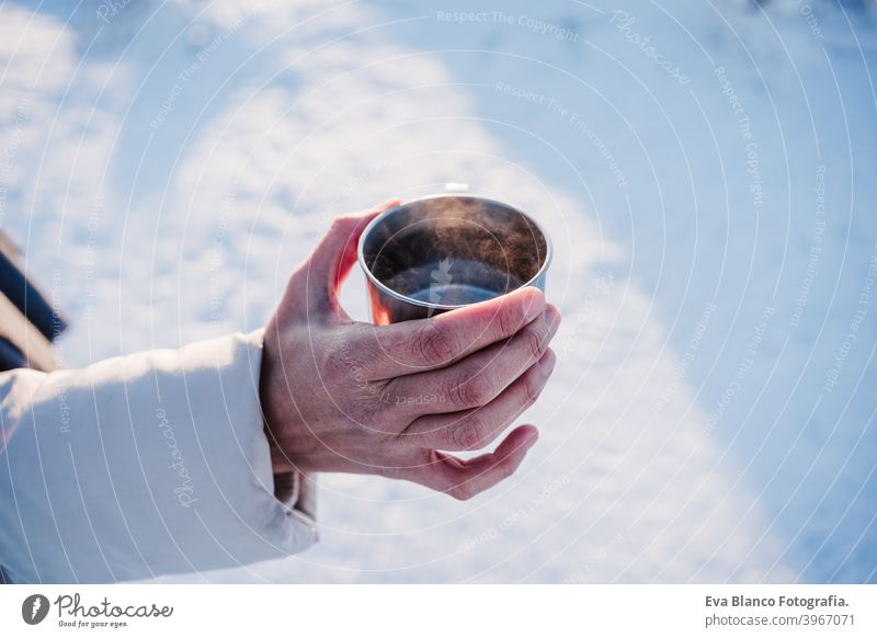 unerkennbar junge Frau bei Sonnenuntergang in verschneiten Berg hält eine Tasse heißen Tee. Reisen und Natur Konzept. Wintersaison heißer Tee Thermoskanne