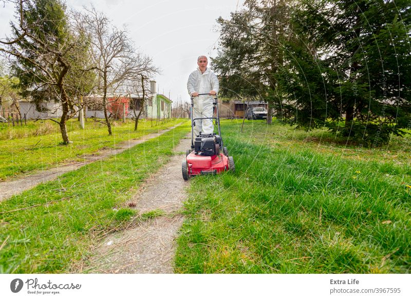 Landwirt in Schutzkleidung mäht Rasen in einem Garten mit einem Benzinrasenmäher Hinterhof Blütezeit botanisch Pflege Schermaschine kultivieren geschnitten