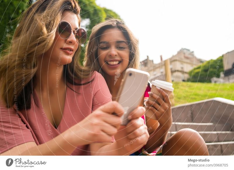 Zwei Freunde benutzen ein Mobiltelefon im Freien. zwei jung Mobile Telefon Lächeln Lachen Freundschaft Lifestyle Freizeit sprechend Spaß Frauen Kommunizieren