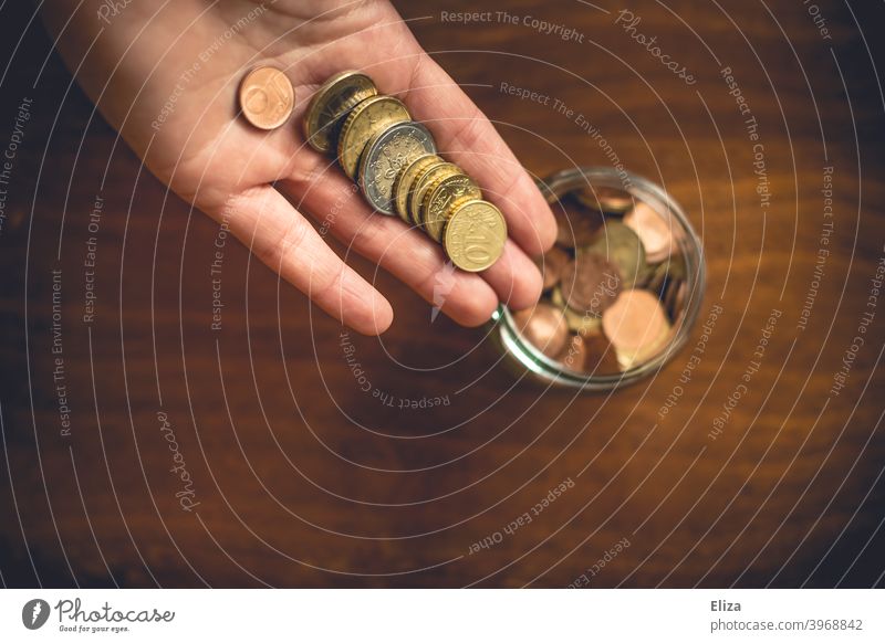 Eine Person legt Geldmünzen in ein Glas. Sparen. Hand Vogelperspektive Spardose Euro Bargeld Münzen halten Kleinvieh sparen Kleingeld Holz sammeln