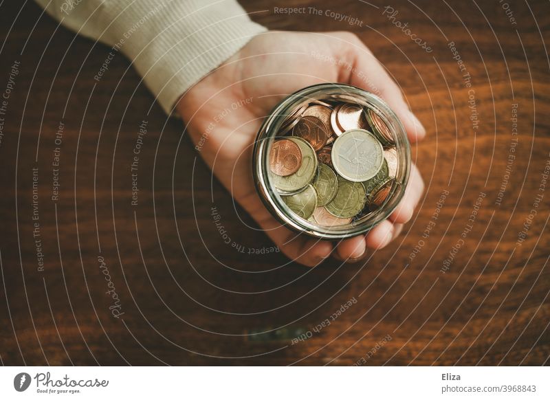 Eine Hand hält ein Glas voller Geldmünzen. Sparen. Vogelperspektive Spardose Euro Bargeld Münzen halten Kleinvieh sparen Kleingeld Holz