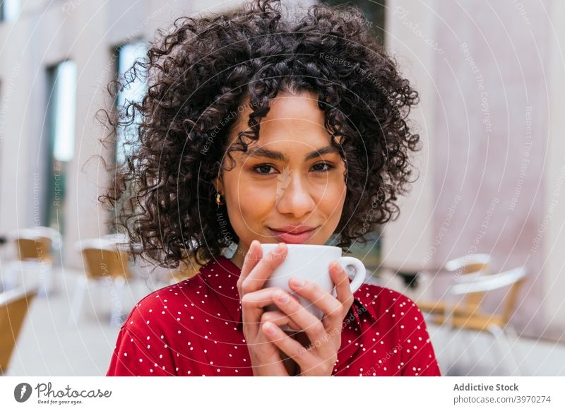 Lächelnde ethnische Frau trinkt Kaffee im Straßencafé trinken genießen Glück Café krause Haare jung Tasse ruhen aromatisch Getränk heiter Lifestyle