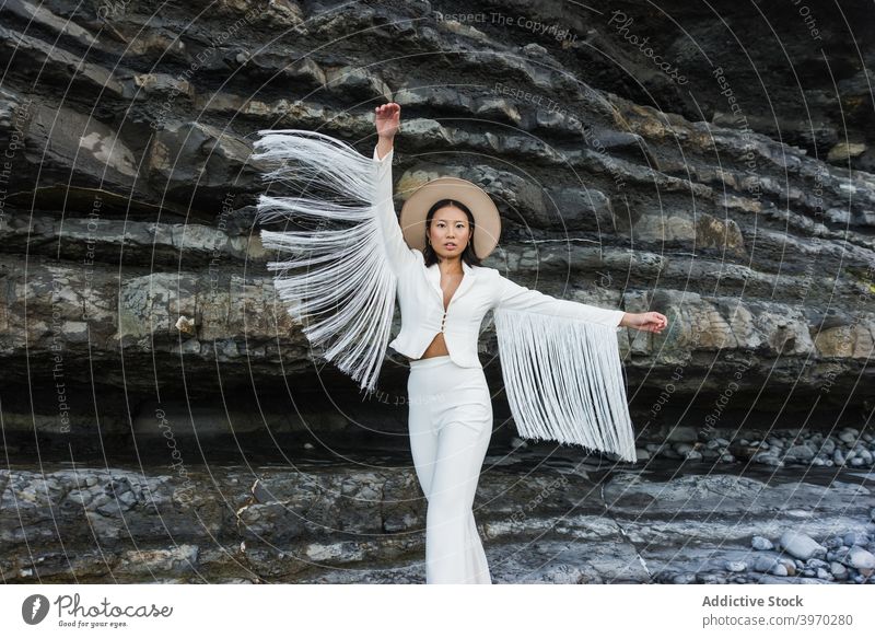 Stilvolle Frau in modischer Kleidung steht in der Nähe von Felsen Mode elegant Outfit weiß Flügel Model Quaste Anzug Hut jung asiatisch ethnisch trendy schlank