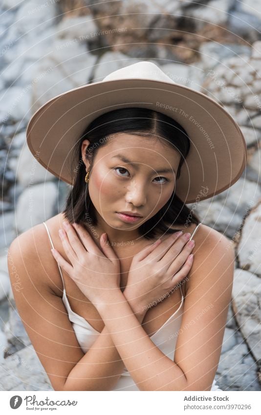 Junge ethnische Frau mit Hut steht auf Steinen Stil Mode Deckung jung Sommer felsig Model asiatisch Kopfbedeckung kalt attraktiv sinnlich rein charmant schlanke