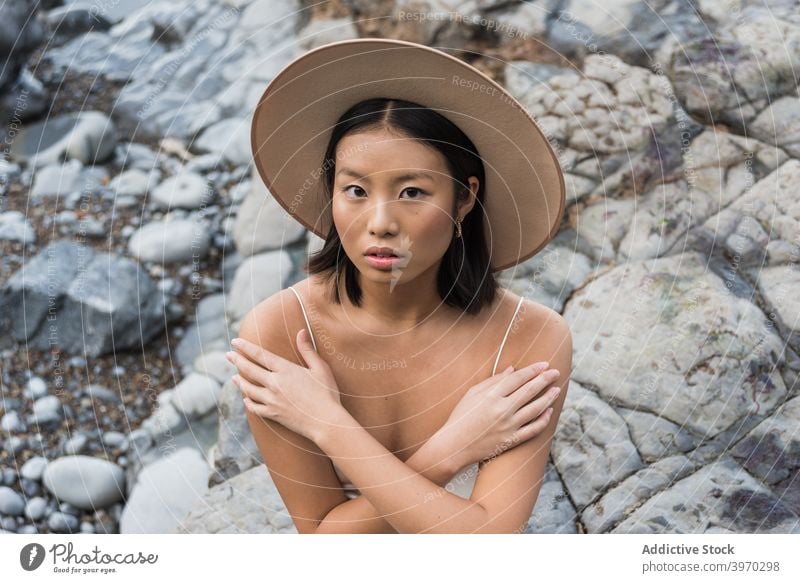 Junge ethnische Frau mit Hut steht auf Steinen Stil Mode Deckung jung Sommer felsig Model asiatisch Kopfbedeckung kalt attraktiv sinnlich rein charmant schlanke