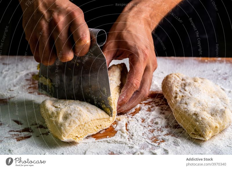 Crop-Bäcker mit Brotteig auf bemehltem Tisch Teigwaren Trennung roh Bäckerei Mann Ball Schaber separat kneten Mehl Prozess Feinschmecker Brotlaib Küchenchef