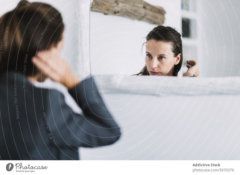 Junge Frau, die ihr Haar vor einem Spiegel zurechtrückt nachdenklich Behaarung ausrichten vorbereiten Morgen formal Routine Reflexion & Spiegelung