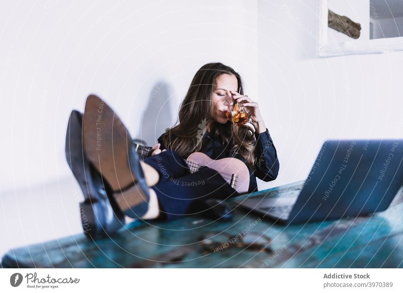 Junge Frau mit Ukulele und Laptop trinken Getränk zu Hause abgelegen ruhen Pause sich[Akk] entspannen Arbeitsplatz genießen jung Apparatur Gerät Lifestyle