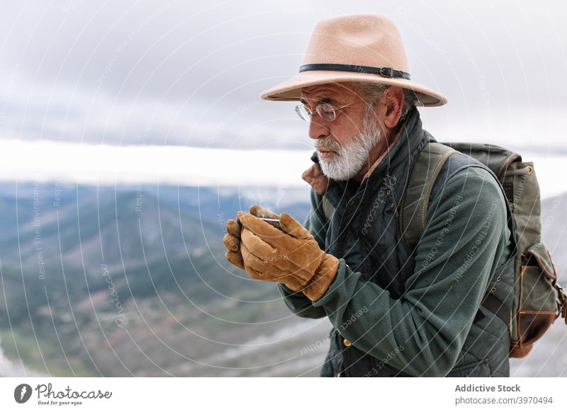 Älterer Reisender trinkt heißen Kaffee im Hochland Mann eingießen Berge u. Gebirge Winter Senior trinken männlich Cacere Extremadura Spanien Oberbekleidung