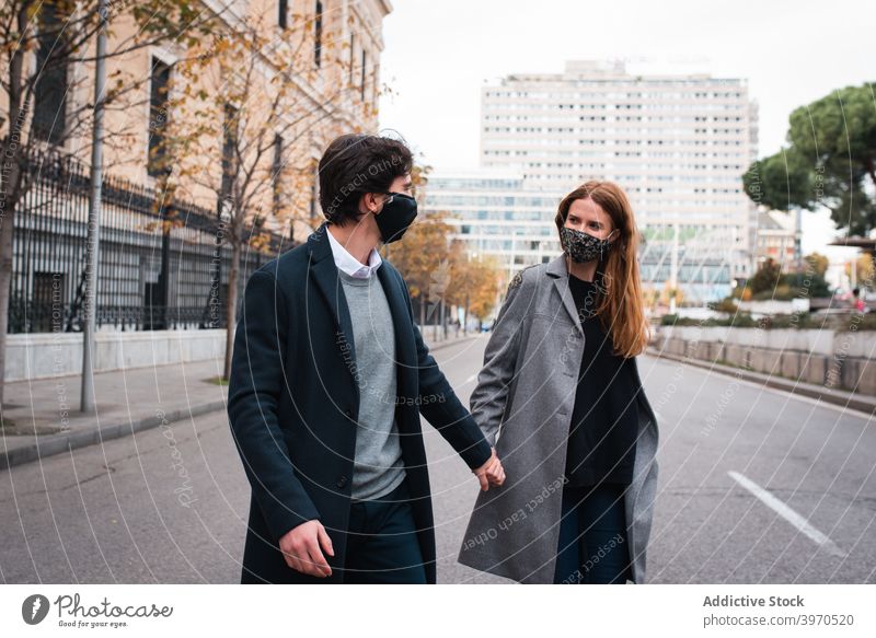 Junges Paar in Schutzmasken zu Fuß auf Stadt Straße Mundschutz urban Glück Zusammensein Händchenhalten behüten Coronavirus neue Normale Liebe Partnerschaft