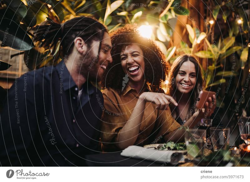 Junge erwachsene Freunde lachen und haben Spaß beim Abendessen Partei mit Telefon offen Fröhlichkeit Smartphone Lächeln junger Erwachsener Afroamerikaner