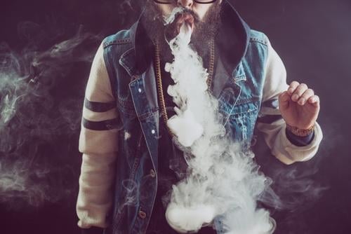 Junger Mann mit Bart, der eine Dampfwolke wirft. Schwarzer Hintergrund. Vaping eine elektronische Zigarette Raps vaping Rauch Erwachsener Cloud cool Lifestyle